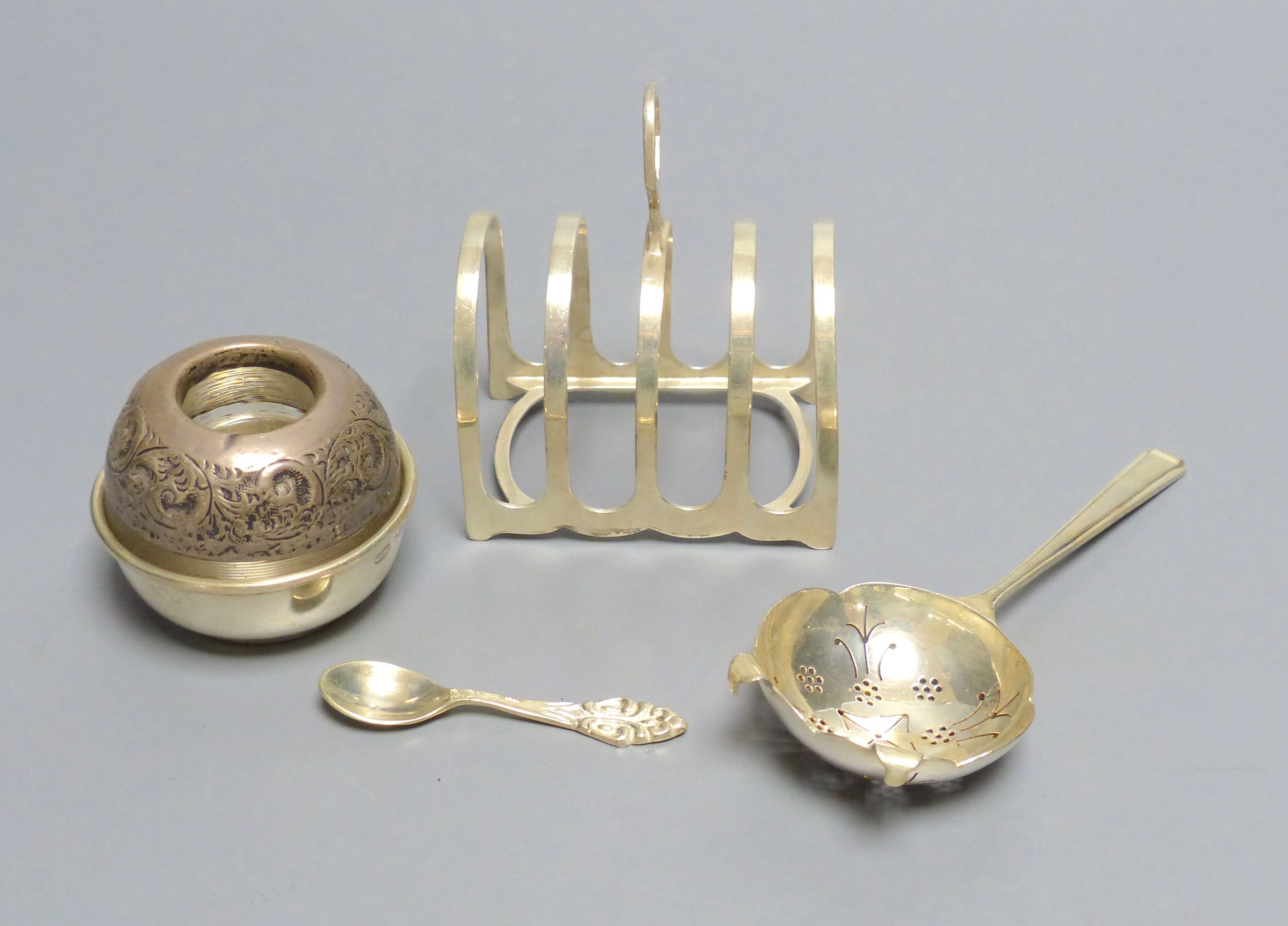 A silver tea strainer, Sheffield, 1964, a George V silver toast rack and an early 20th century silver mounted match tidy,